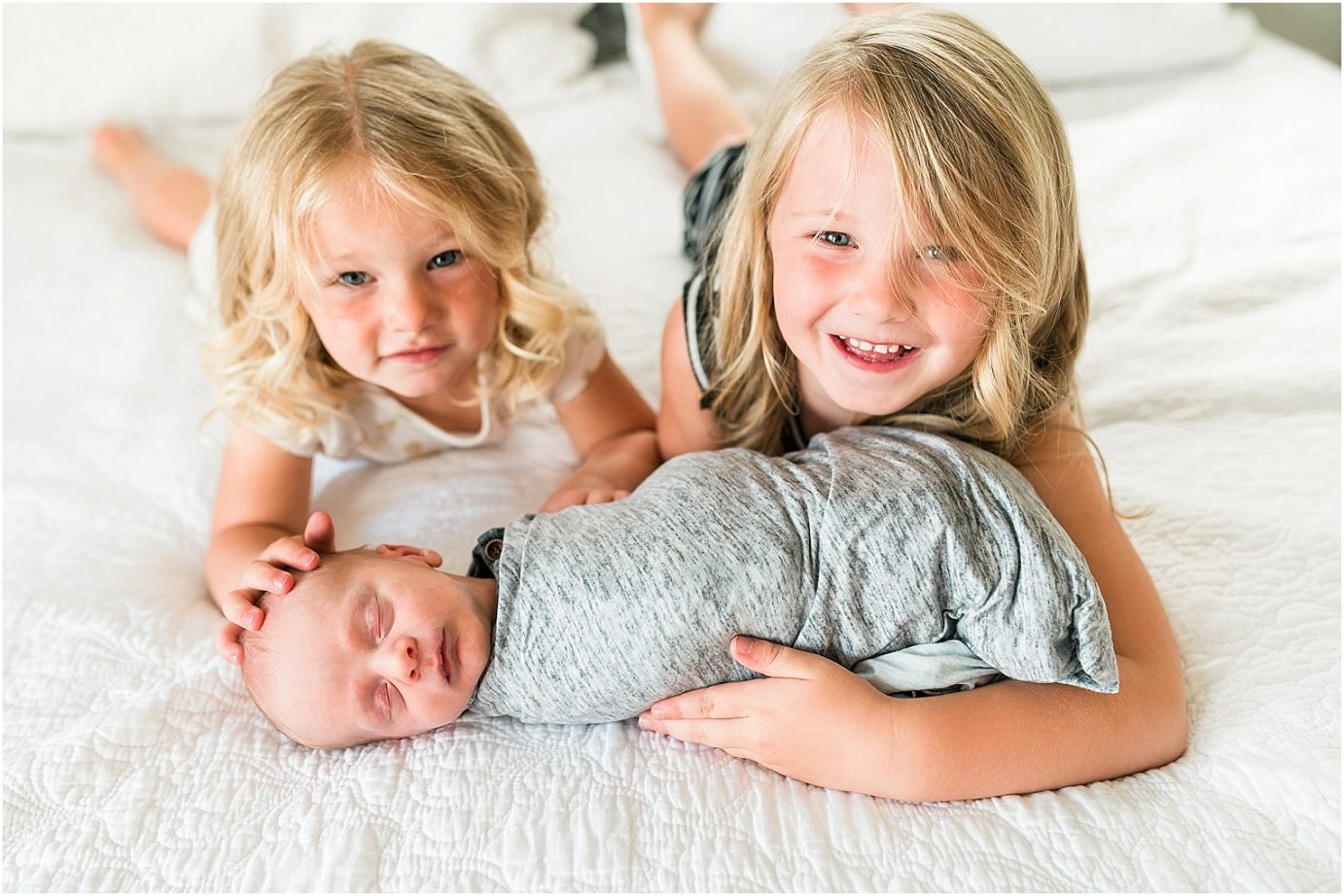 sisters with baby brother on bed